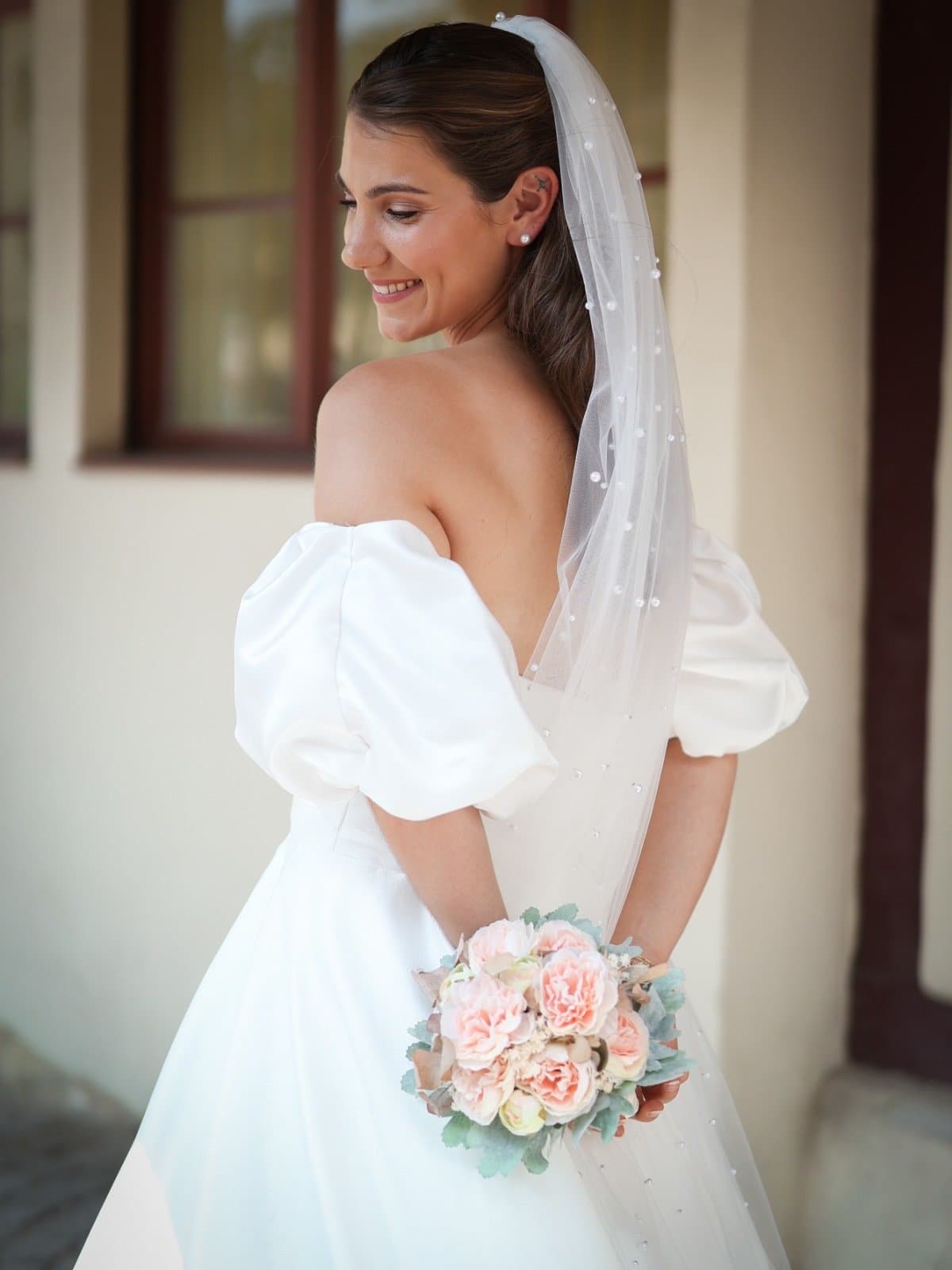 Braut im Off-Shoulder-Kleid mit Puffärmeln und Perlenschleier, rosafarbener Brautstrauß, Neue Kollektion bei Brautmode Liebesgeschichte