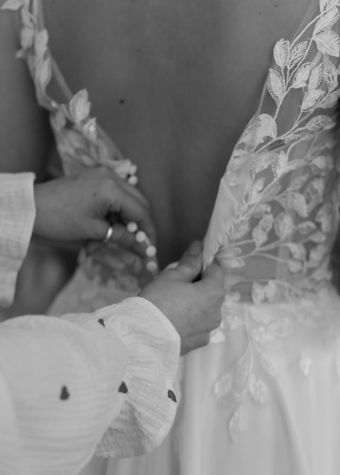 Inhaberin knöpft Brautkleid mit Blätterapplikation zu — Detail-Aufnahme Brautmode Liebesgeschichte