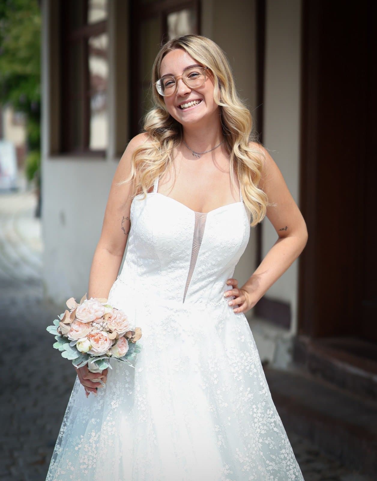 Braut lacht mit Brautstrauß in glitzerndem A-Linien-Kleid mit Herzausschnitt, Shooting von Brautmode Liebesgeschichte